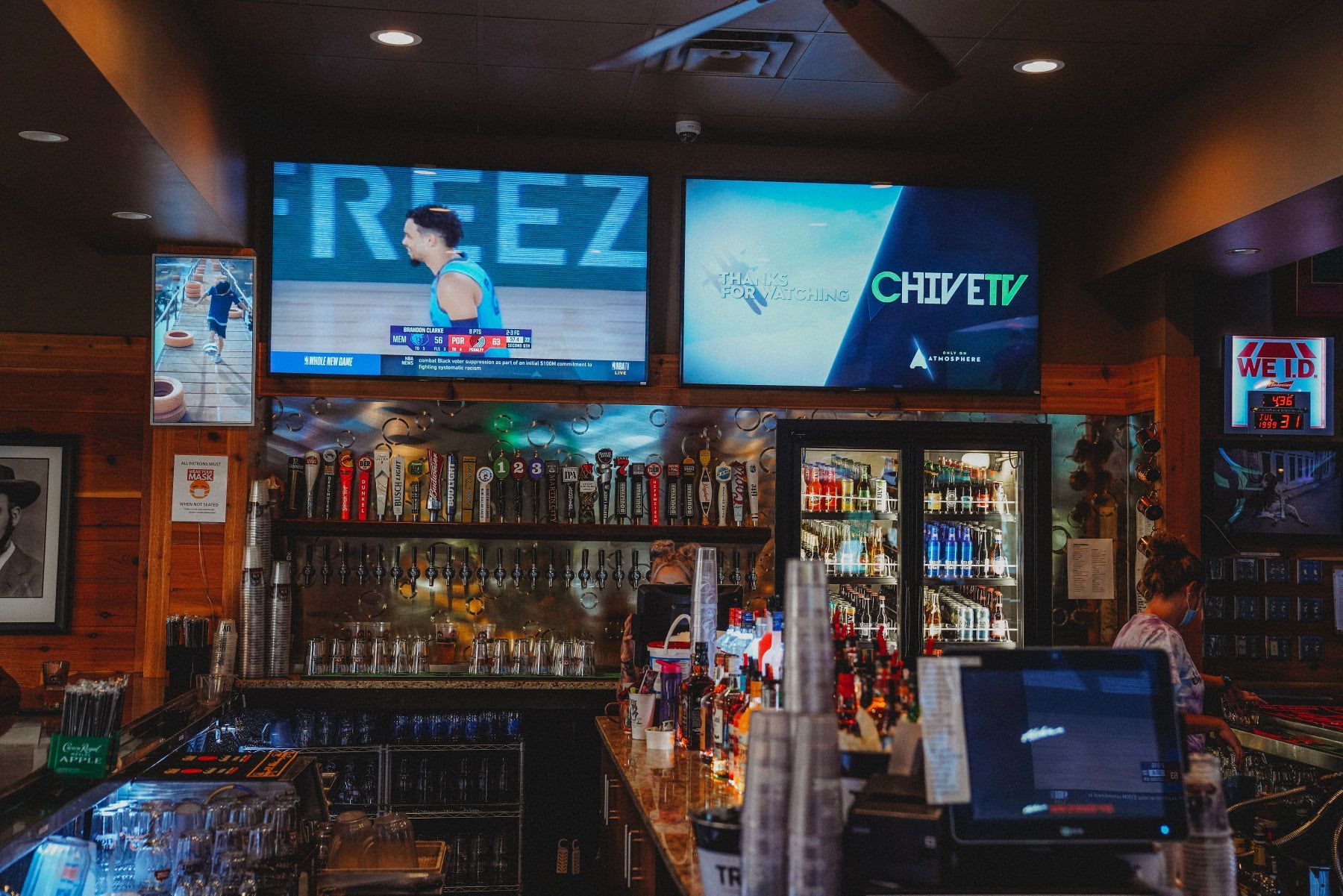 Bar interior with multiple TVs displaying sports and programming, behind the bar, and a bartender.