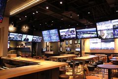 Interior of a sports bar with many TVs displaying various games. Wooden tables, bar stools, and a bar area are visible.