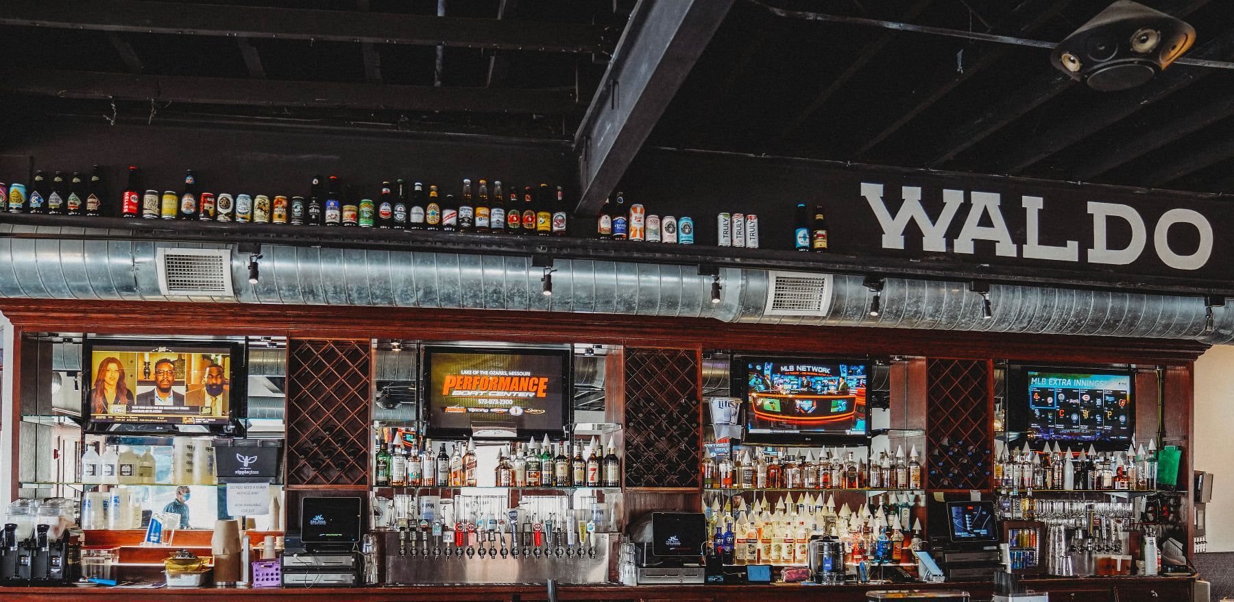Bar interior with bottles of liquor on shelves, TVs, and the word WALDO.