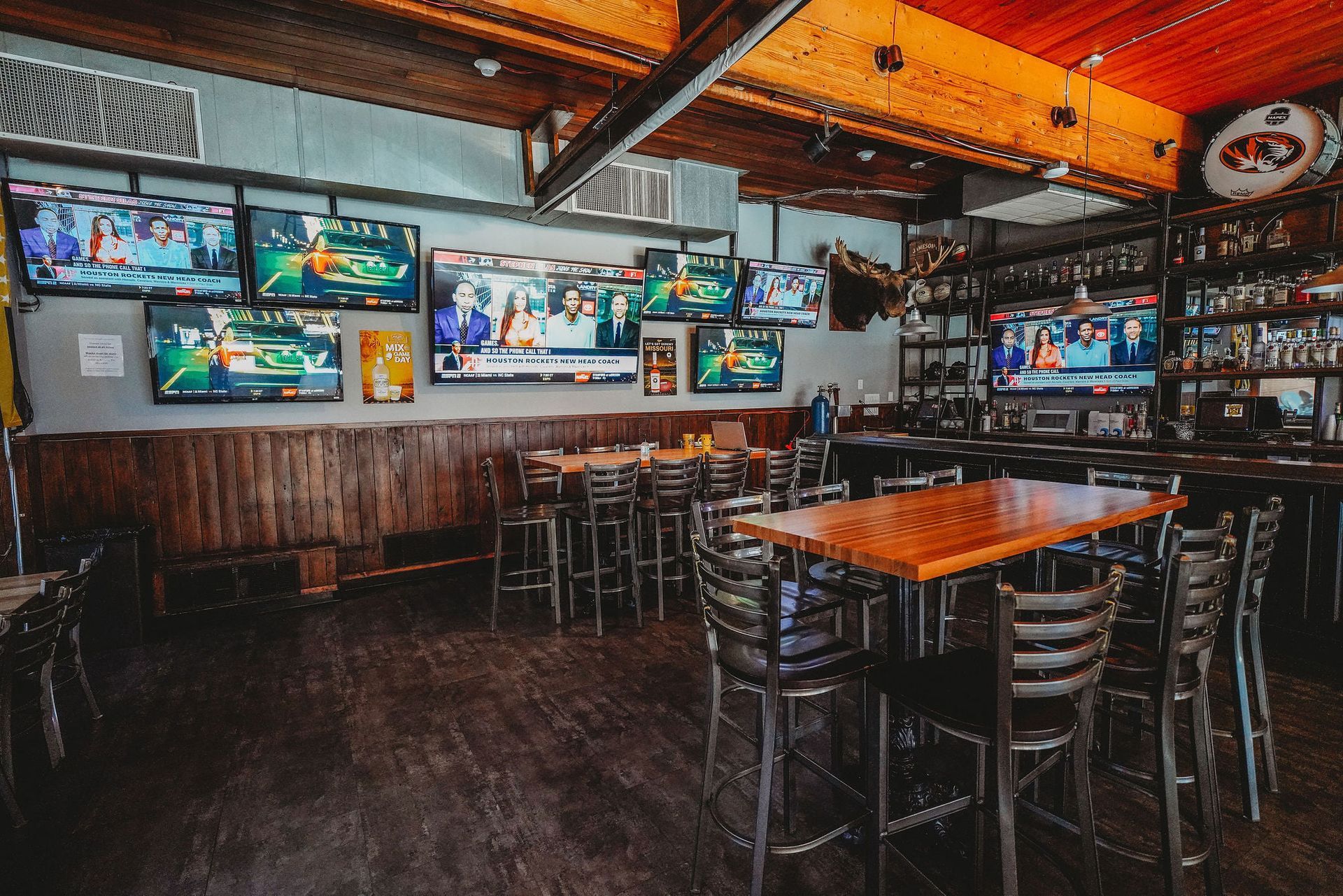 Bar interior with multiple TVs showing various programs, tables, and bar stools.