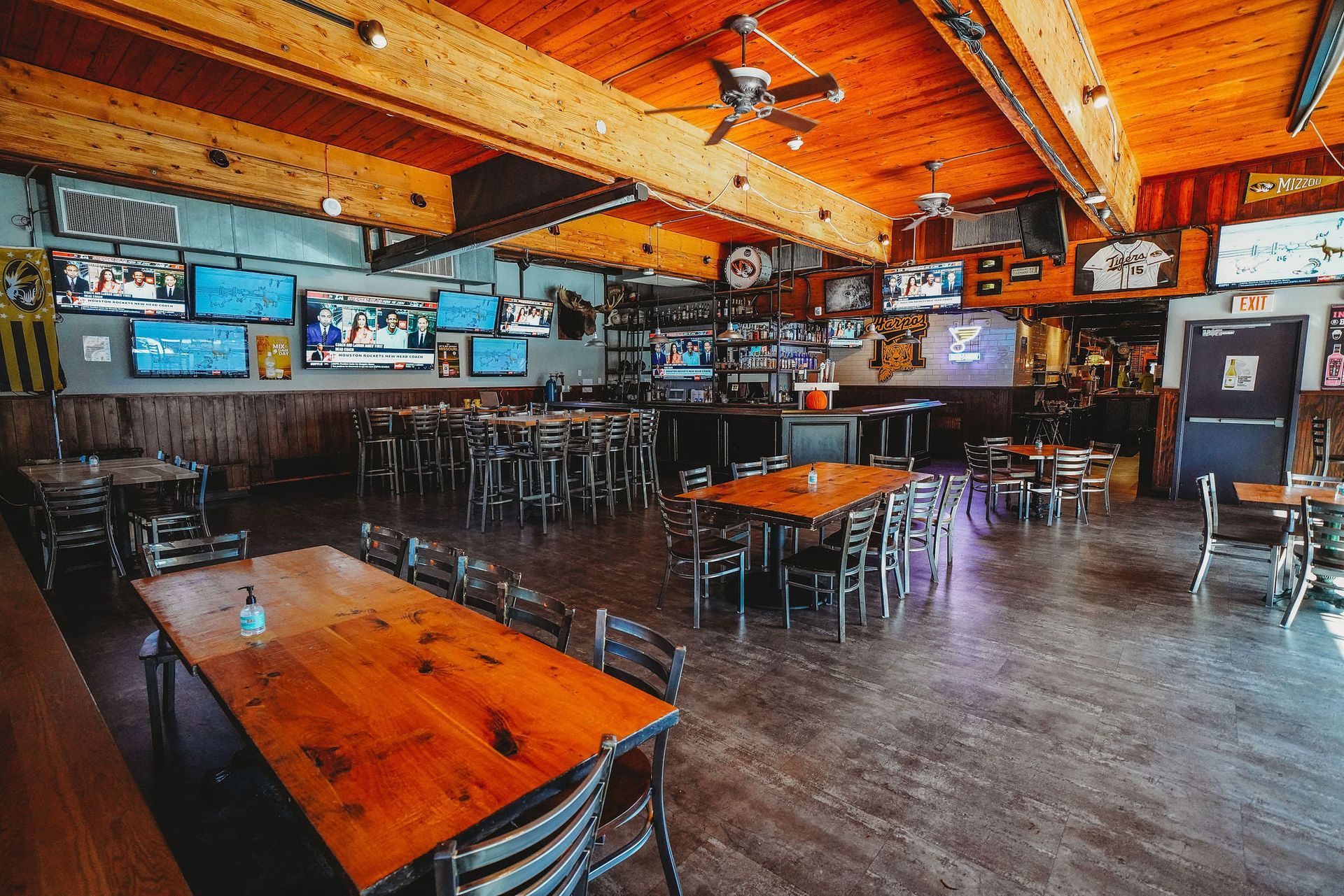 Interior of a sports bar with wooden tables, TVs on walls, and a bar area in the background.