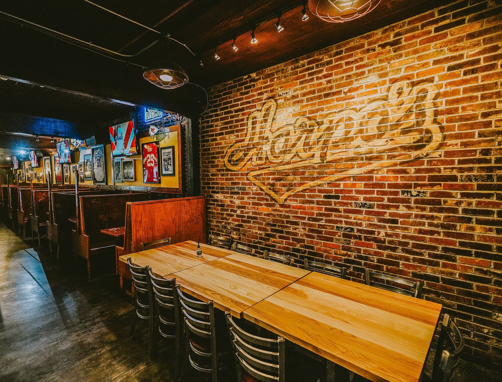 Interior of a brick-walled bar with wooden tables, booths, and a neon sign.