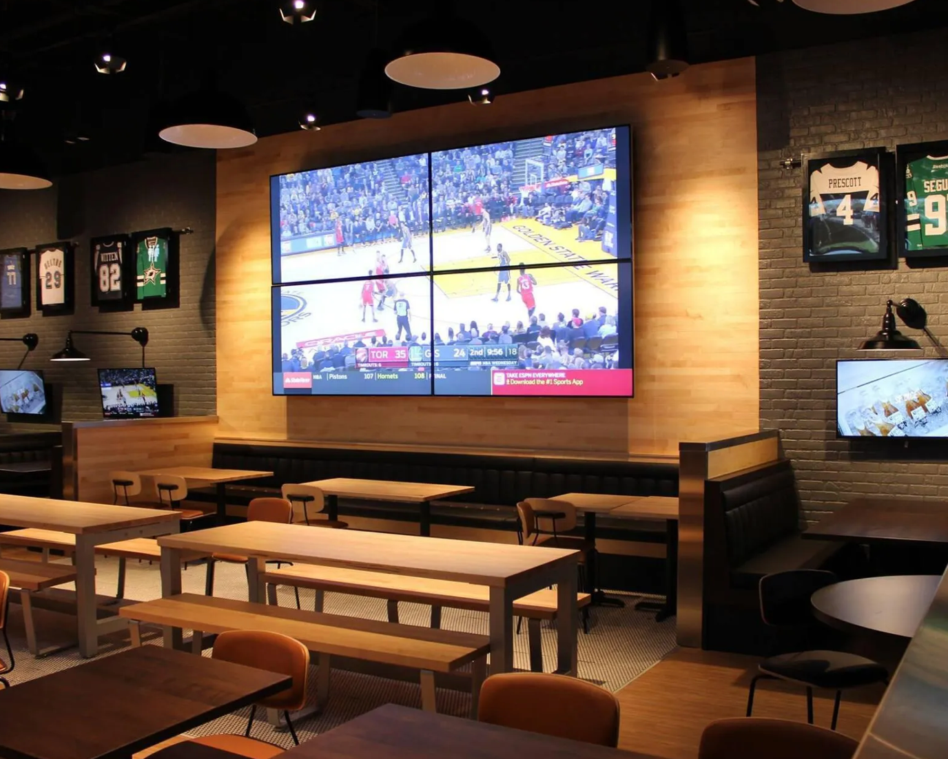 Restaurant interior with large screens showing sports, tables, and bench seating.