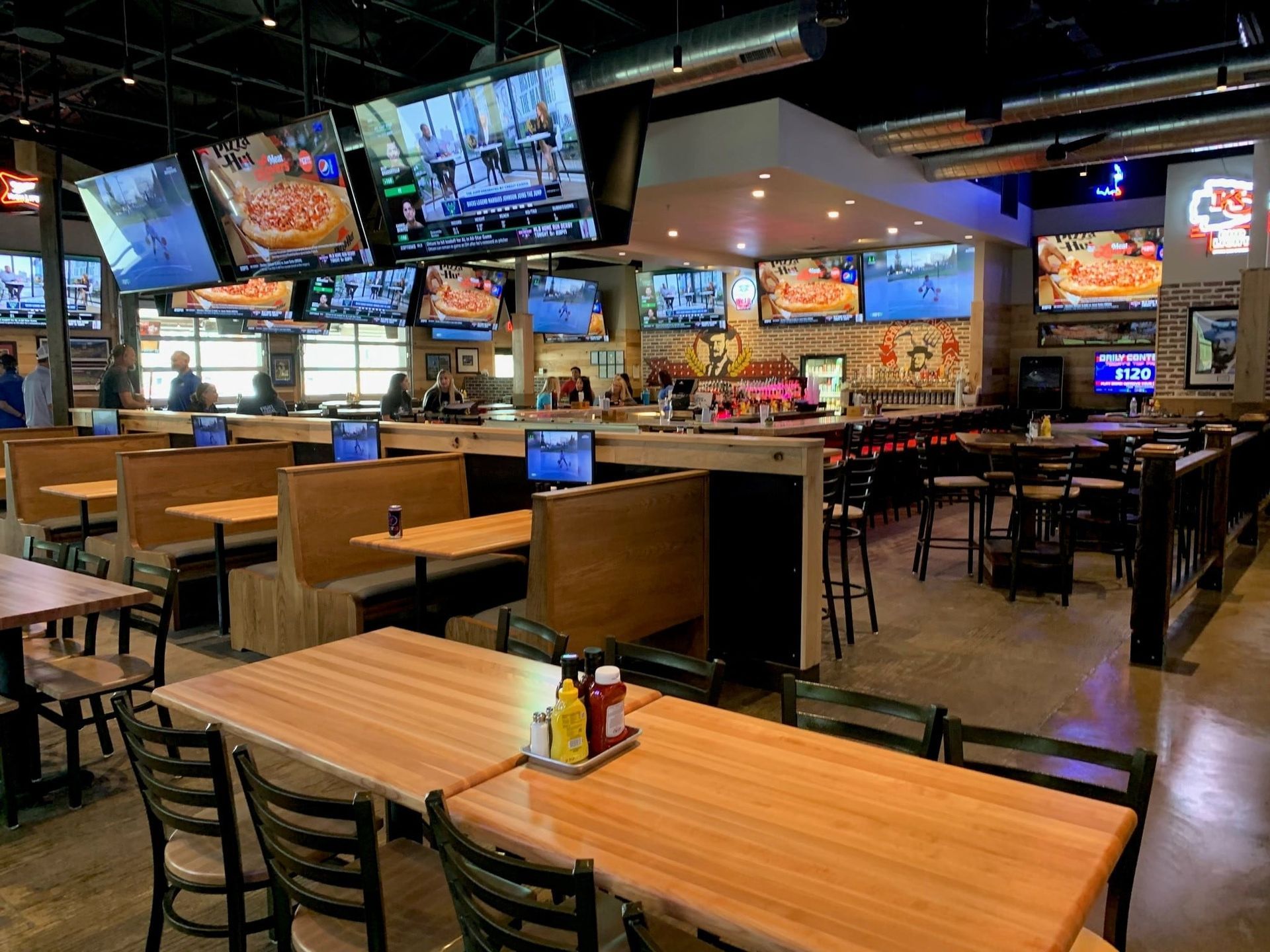Inside a sports bar, tables, booths, bar seating, many TVs displaying games.