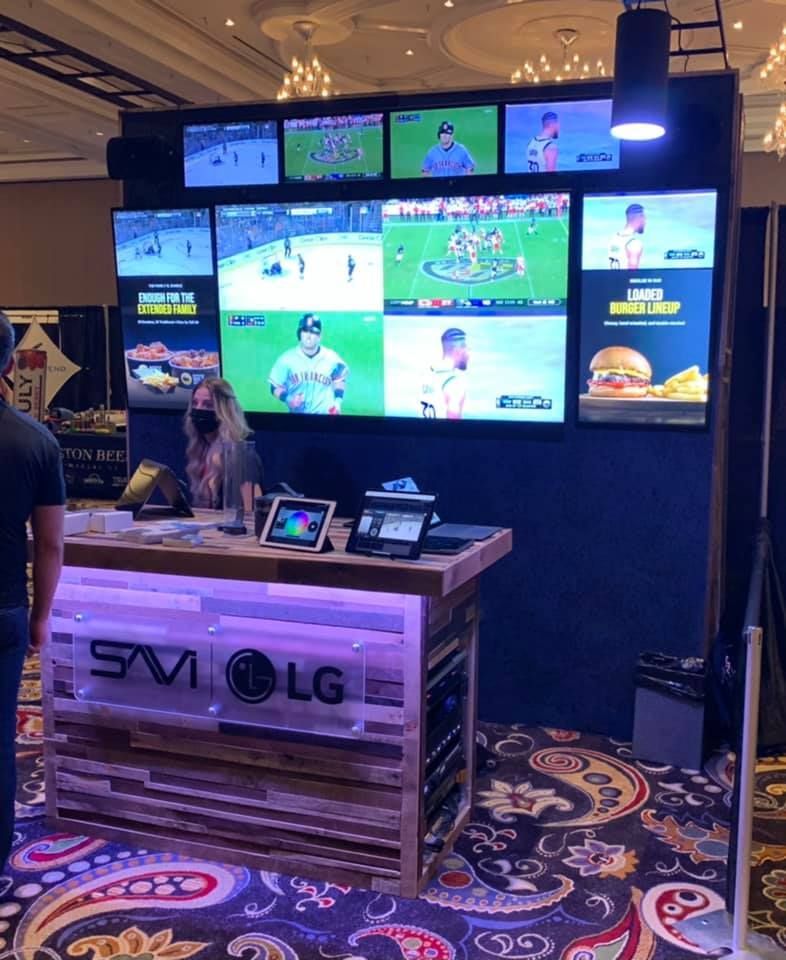 Display booth with multiple TVs showing sports, a counter with a person, and a digital menu.