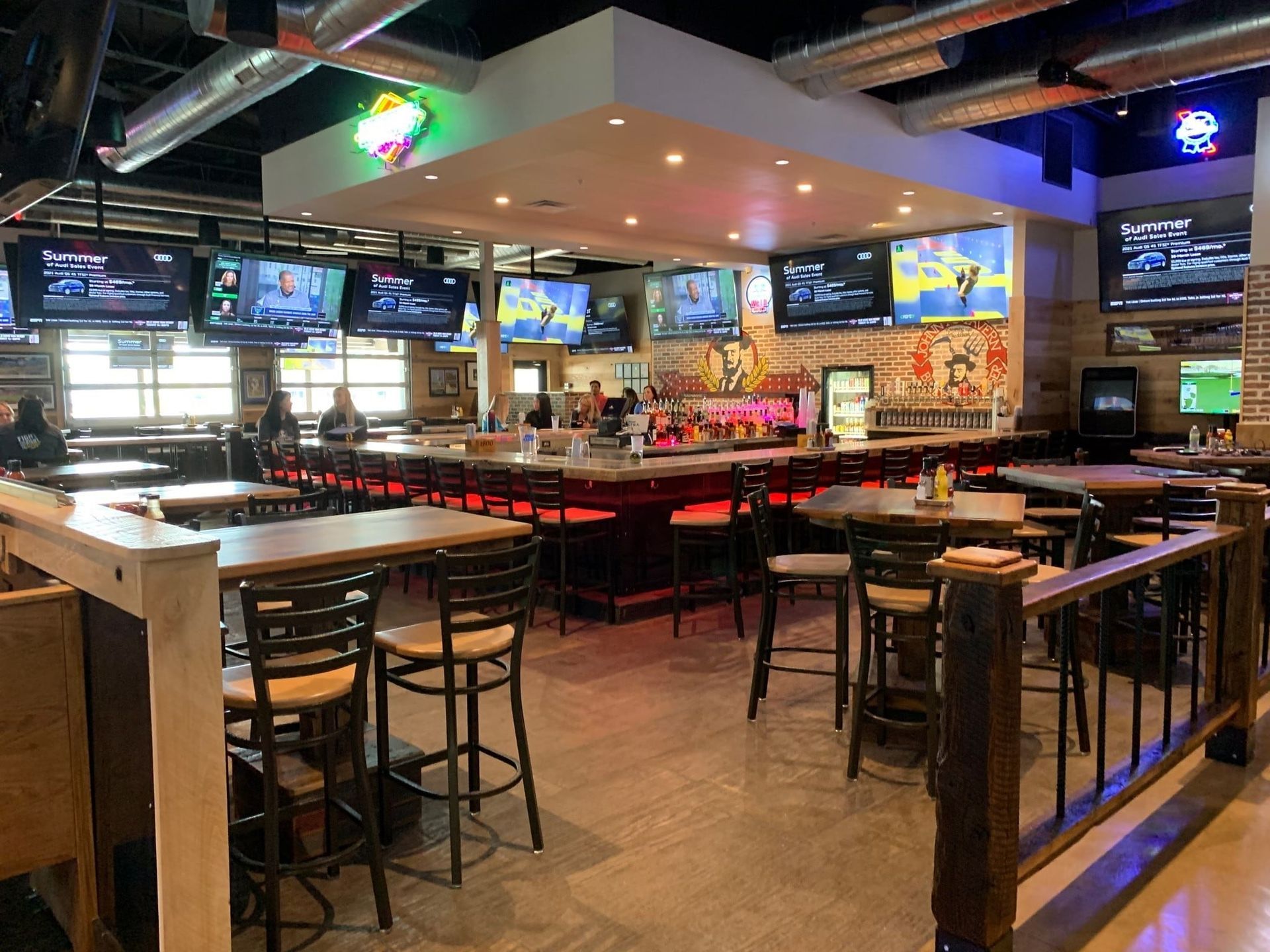 Inside a sports bar, TVs surround a bar with red lighting. Tables and chairs are in the foreground.