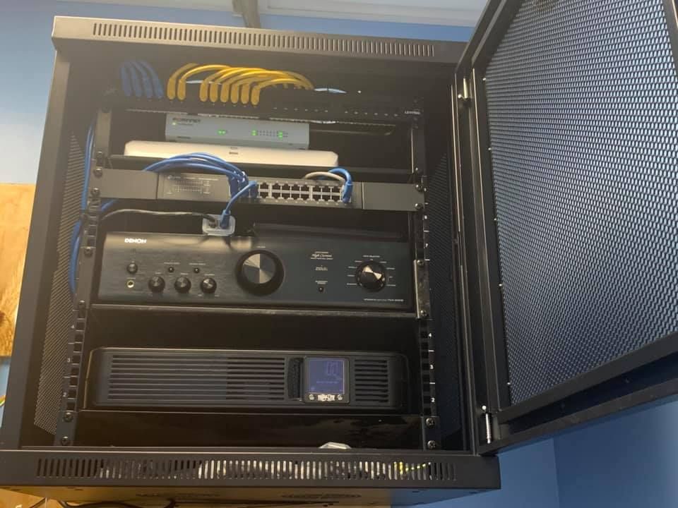 Black network rack cabinet with equipment inside. Cables in blue and yellow. Cabinet door open.
