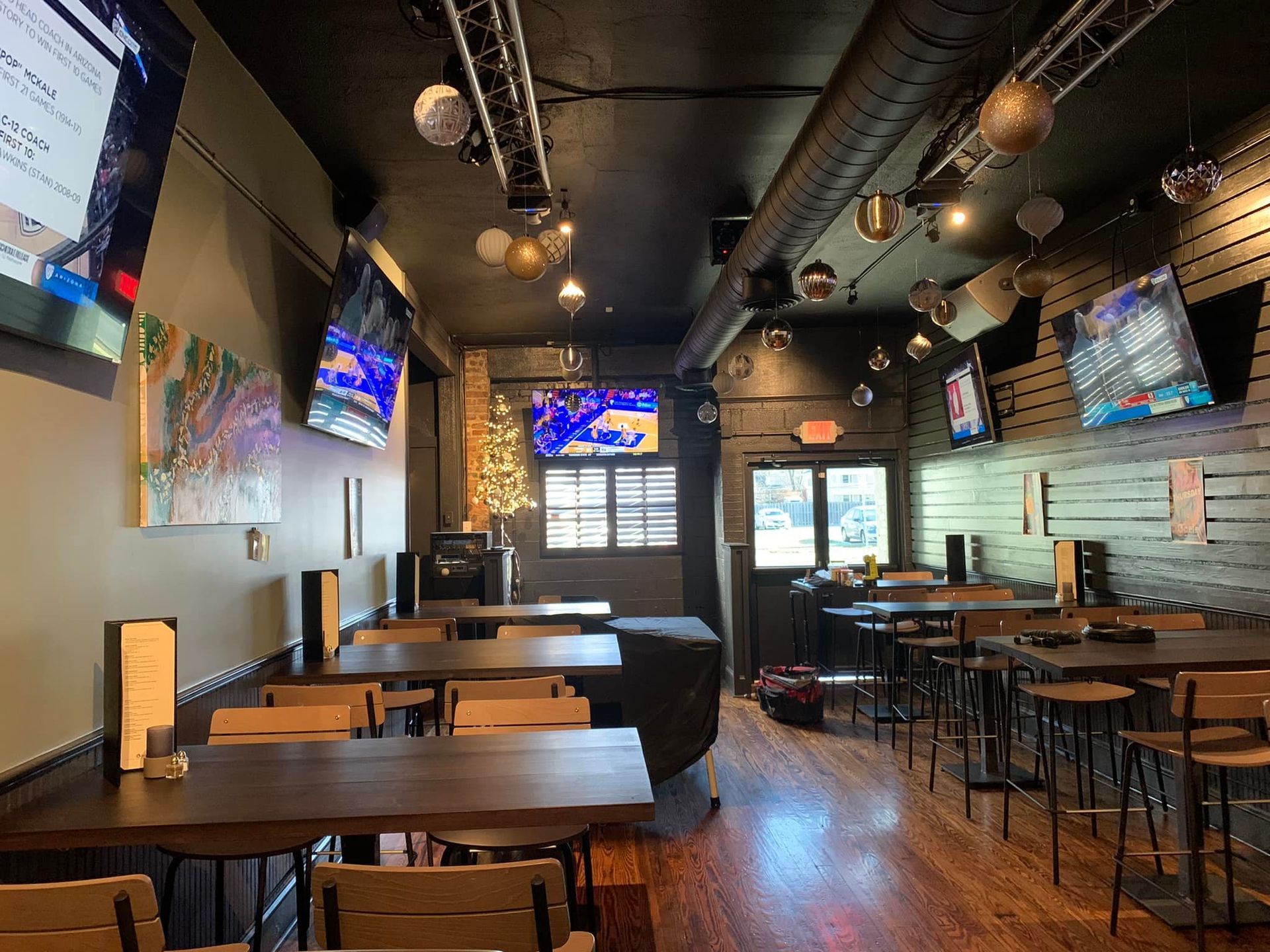 Interior of a bar with tables, chairs, TVs, and decorative lighting on dark walls and ceiling.