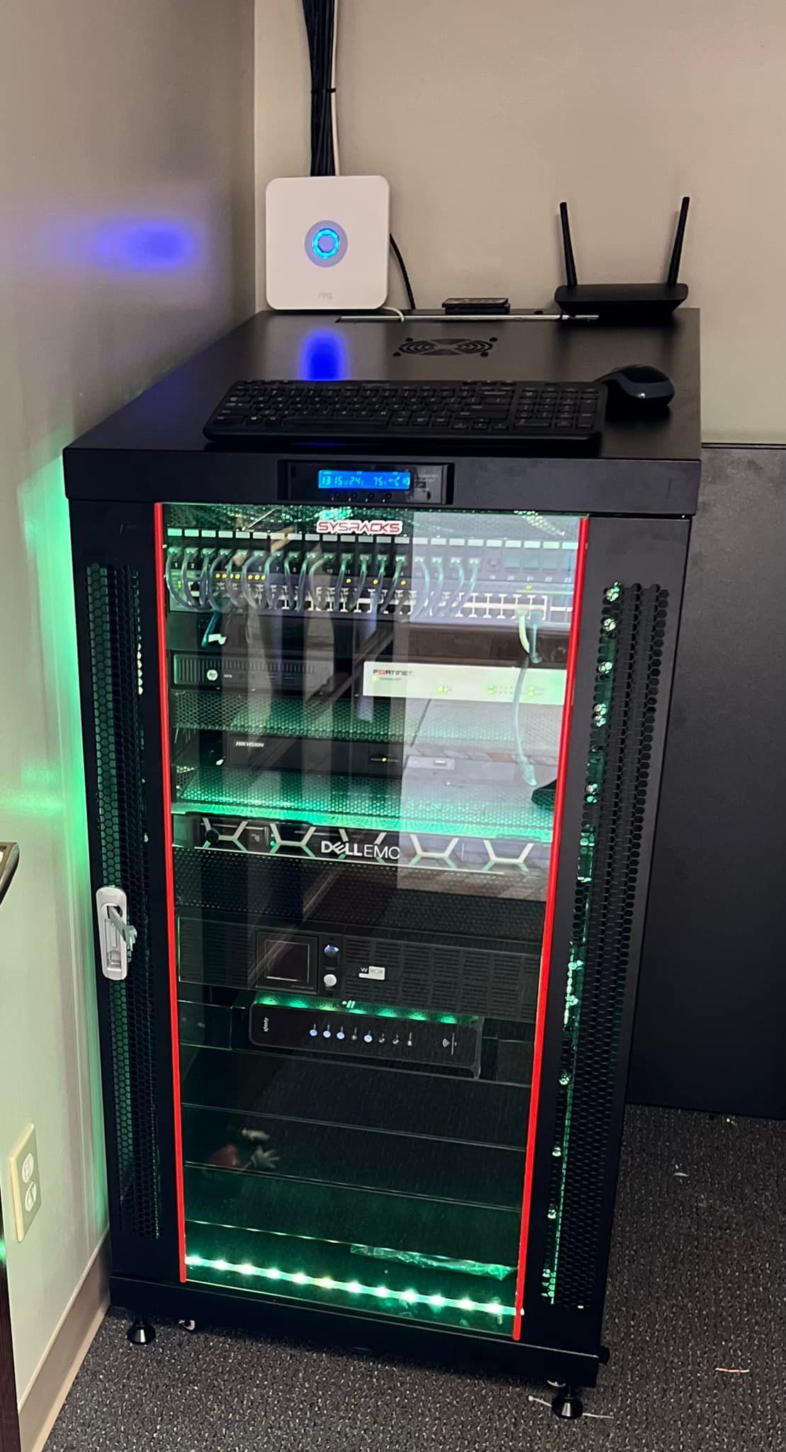 Server rack in a room with a desk above it; green and blue lights illuminate the equipment.