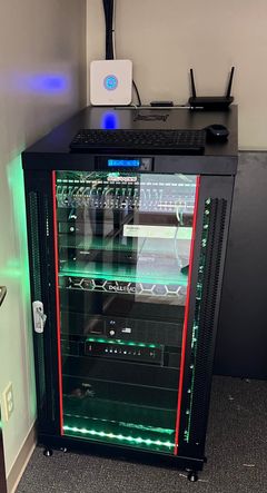 Server rack in a room with a desk above it; green and blue lights illuminate the equipment.