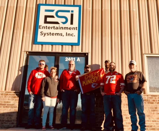Group of people in front of ESI building, some wearing Kansas City Chiefs gear, holding a Chiefs banner.
