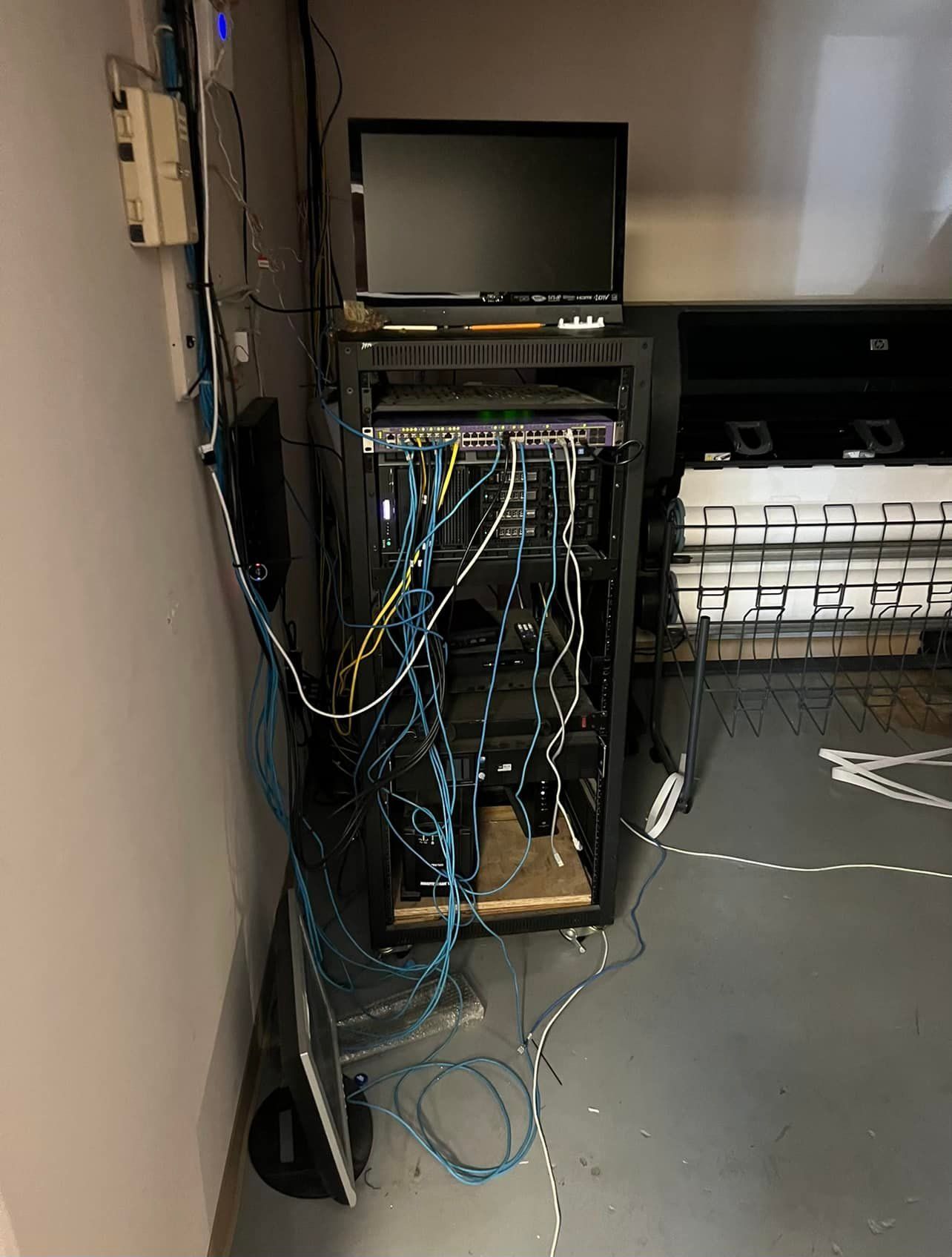 Server rack in a corner with tangled network cables and a monitor.