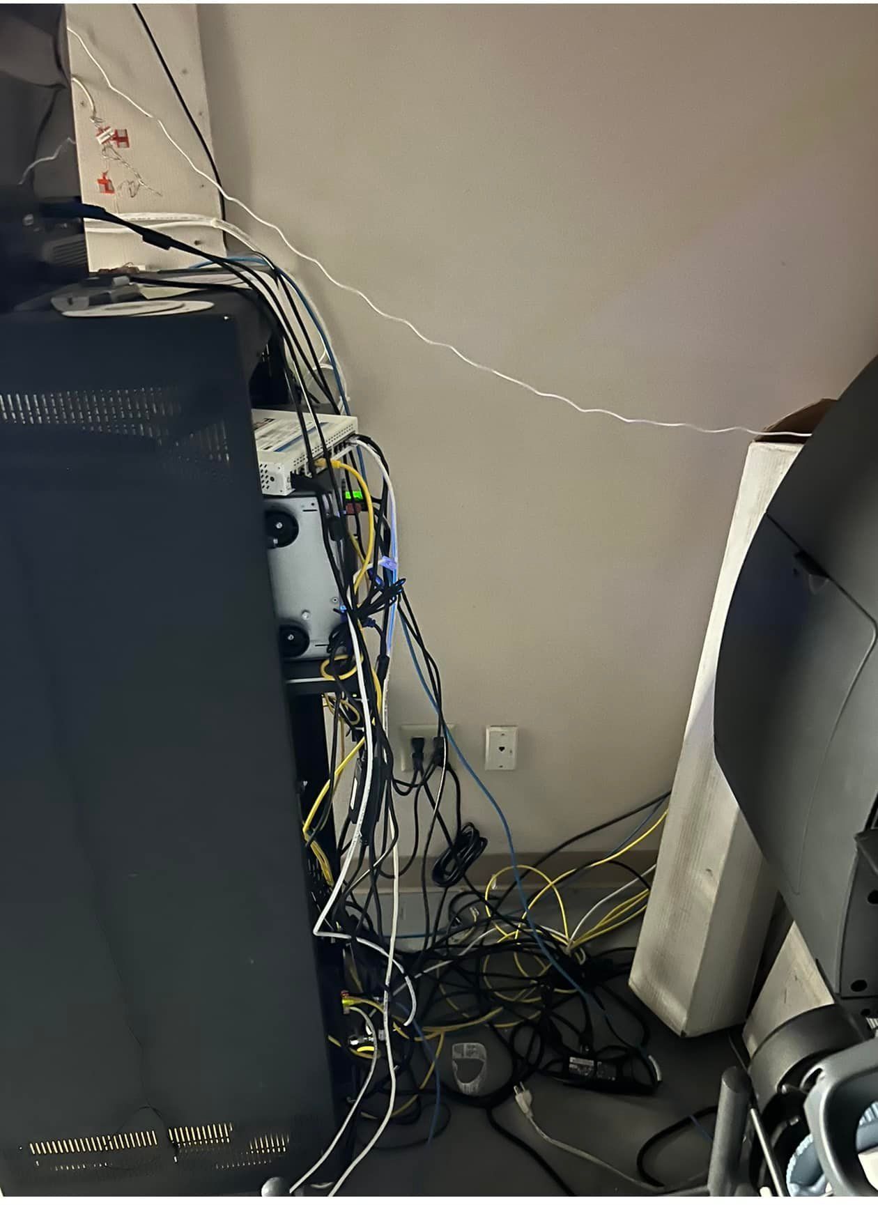 Tangled cables and equipment against a wall, next to a tall black speaker and lighting equipment.