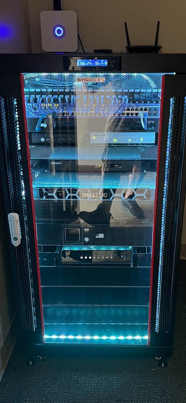 A lit server rack with glass doors, lights, and networking equipment, inside a dark room.