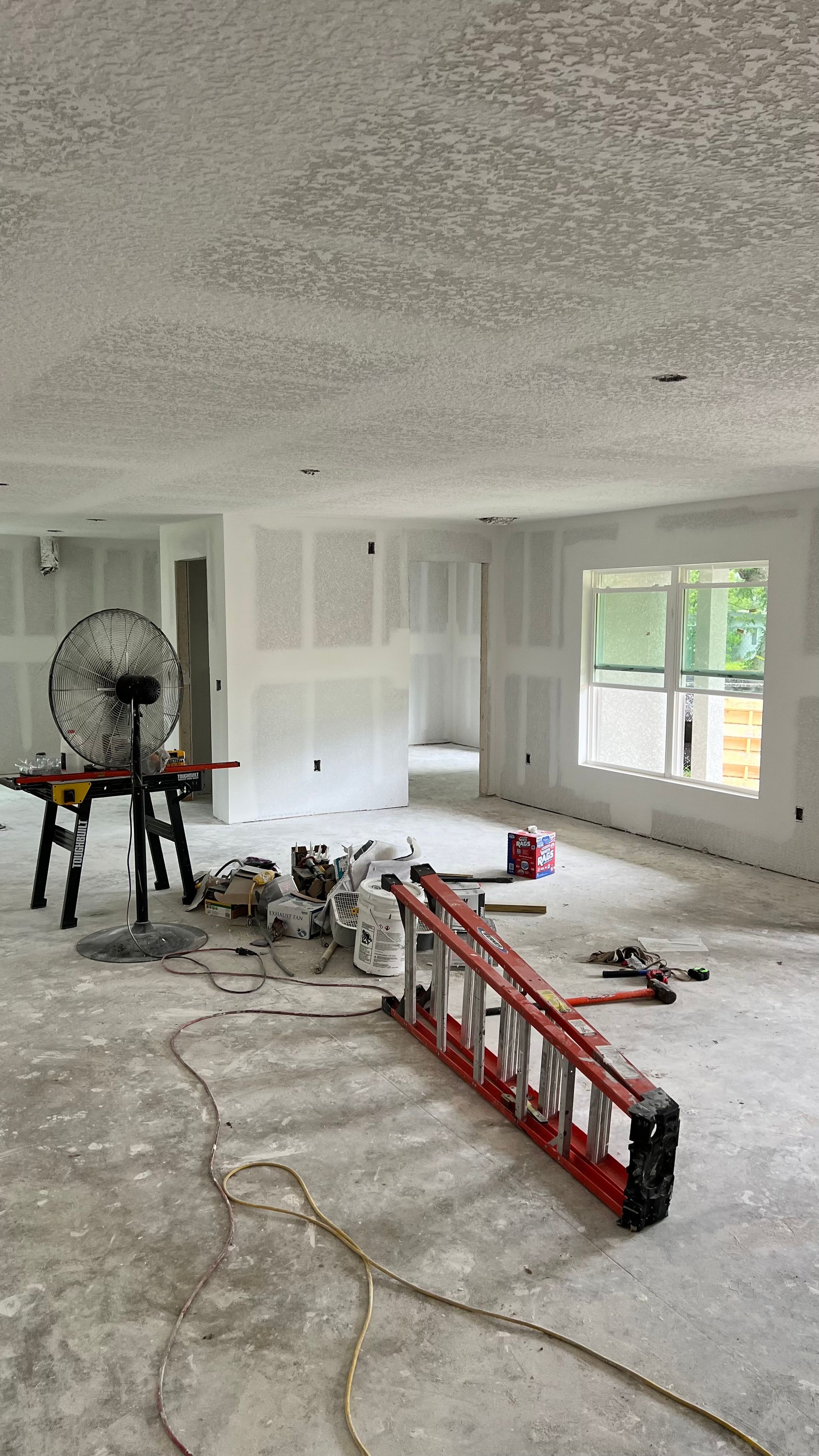 An empty room with a ladder and a fan on the floor.