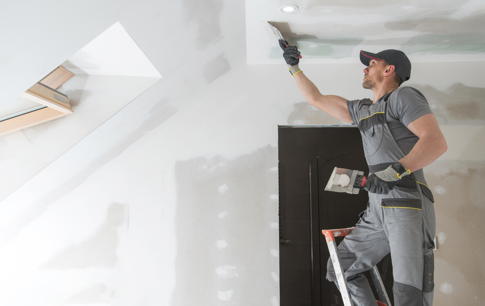 A man is standing on a ladder and plastering a ceiling.
