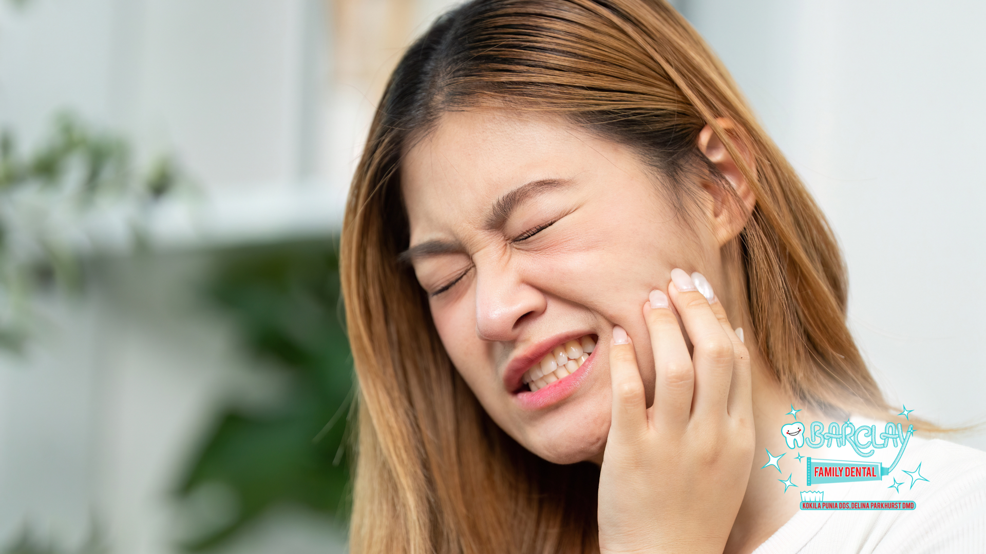 Woman clutching her cheek with a pained expression, likely toothache, indoors.