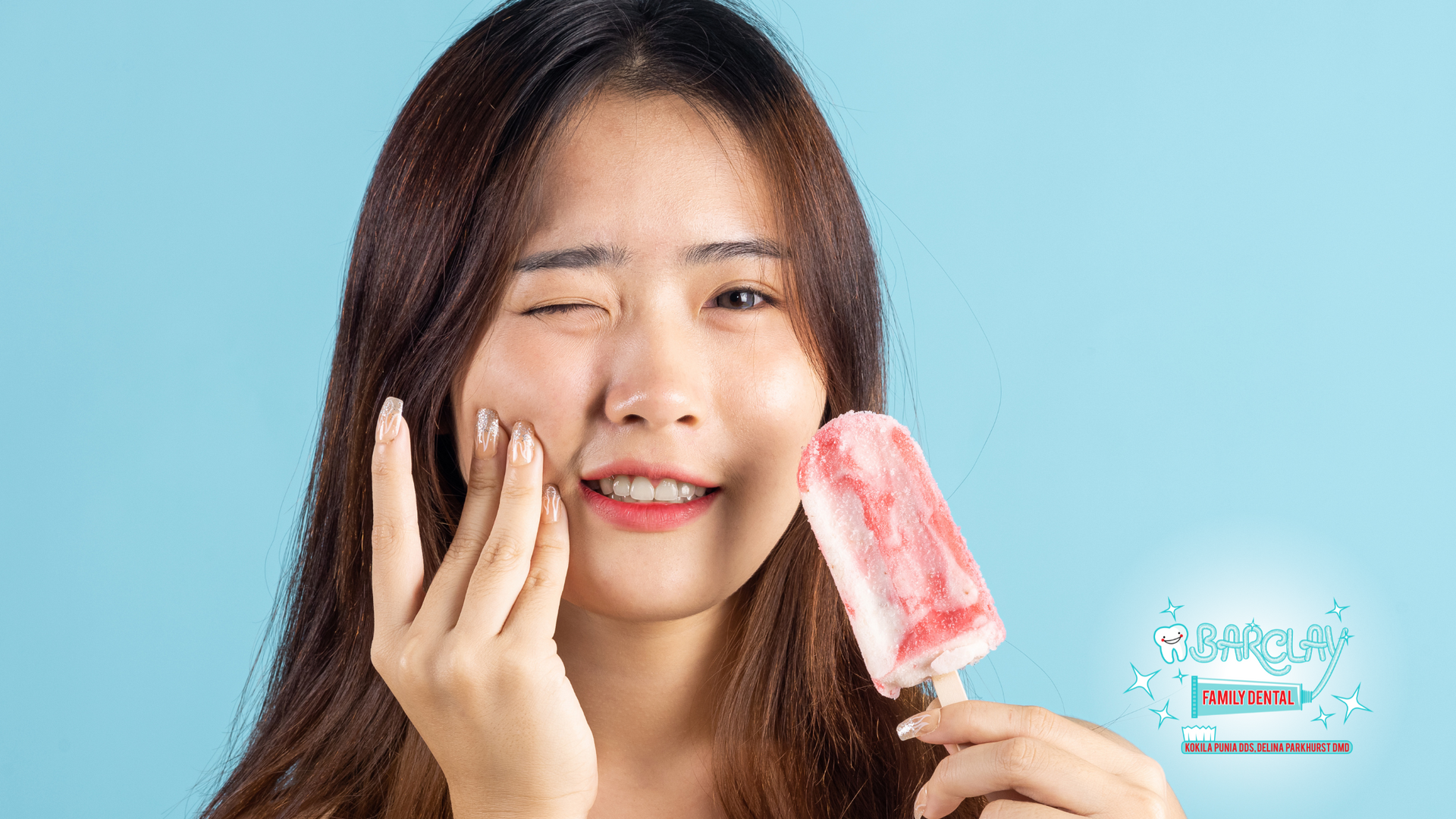 Woman winking, holding red popsicle, smiling; light blue background.