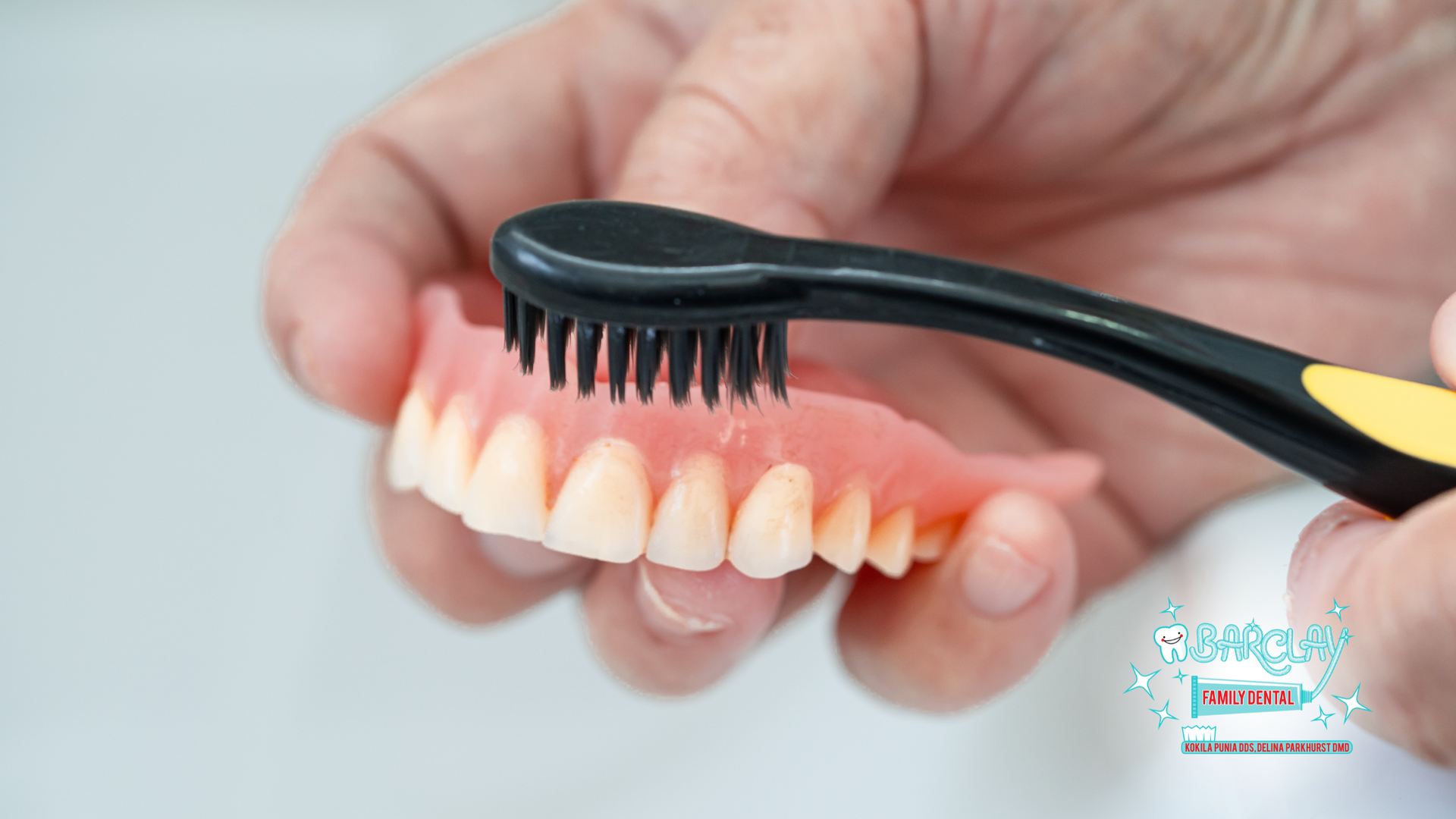 A person is brushing a denture with a toothbrush.