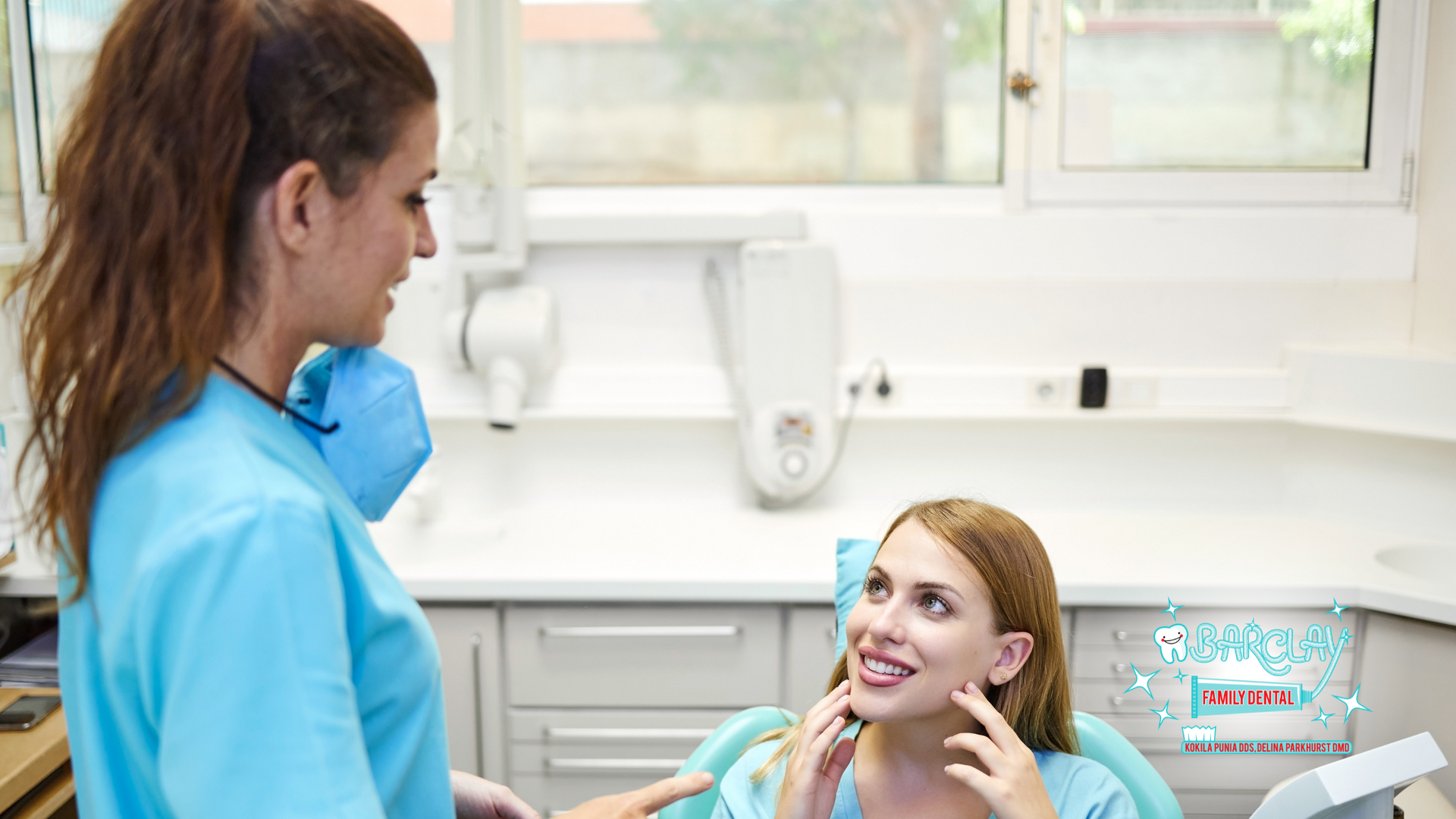 A dental assistant in scrubs speaks to a patient in a dentist's chair. Light blue decor and equipment.