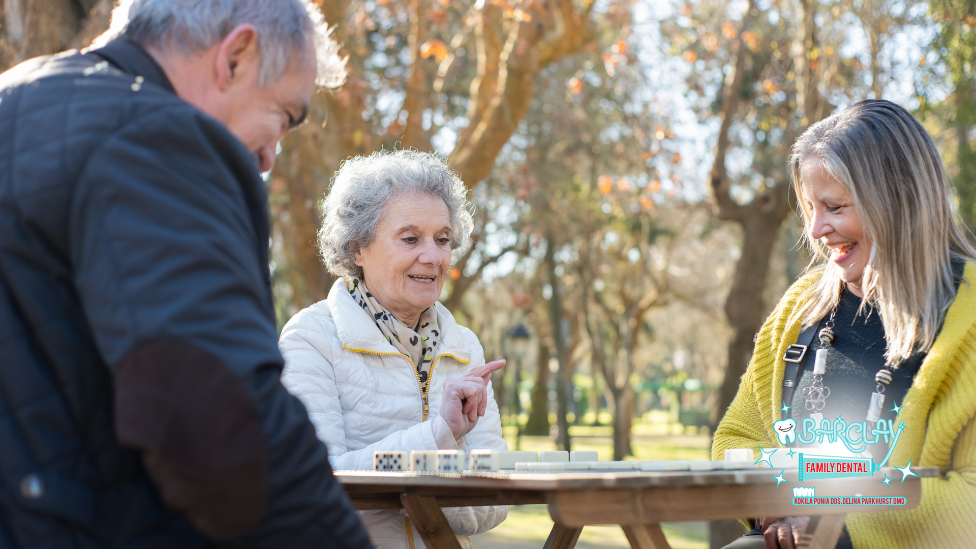 A group of people are sitting at a table in a park playing a game.