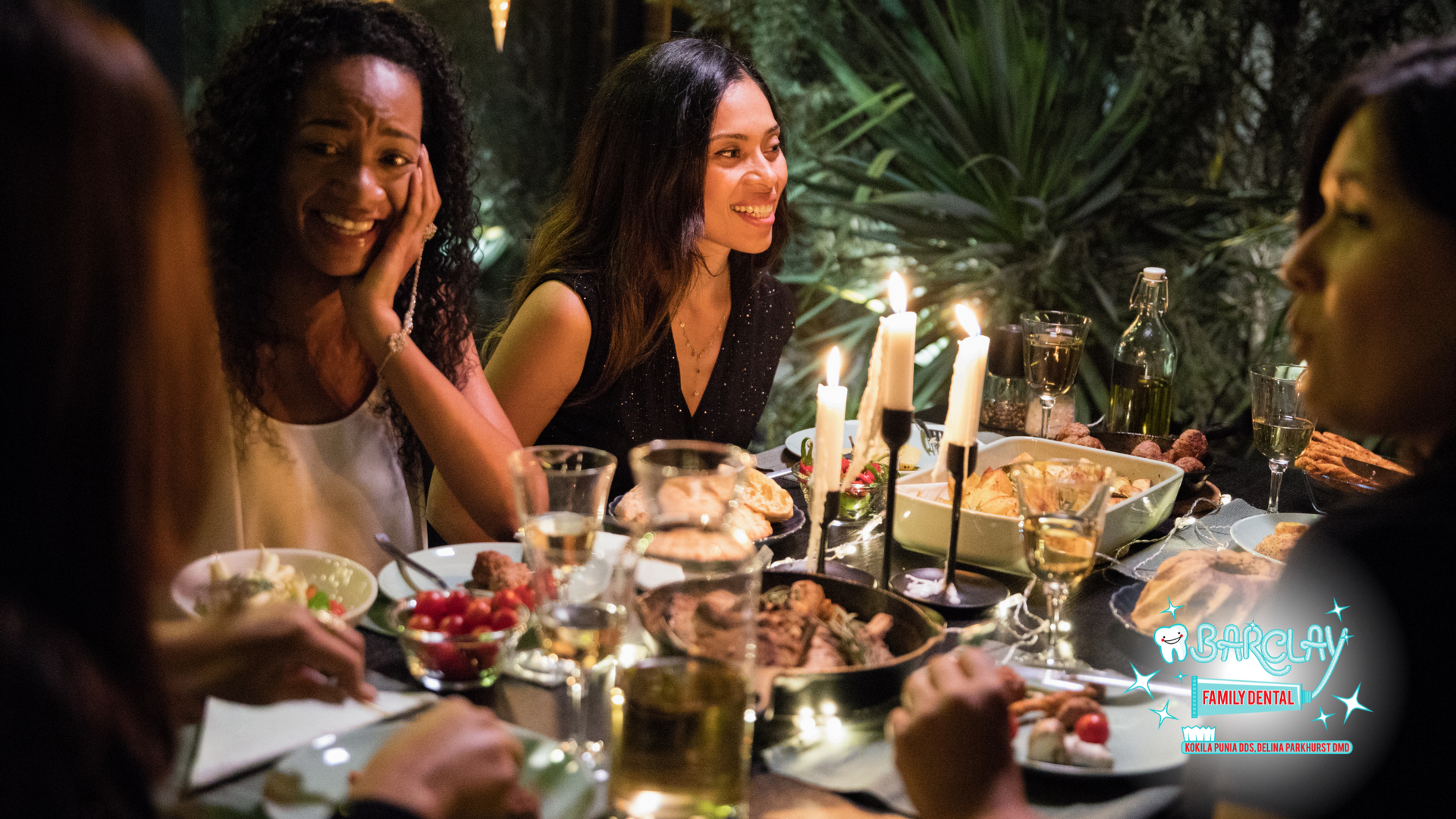 A group of women are sitting at a table with plates of food and candles.