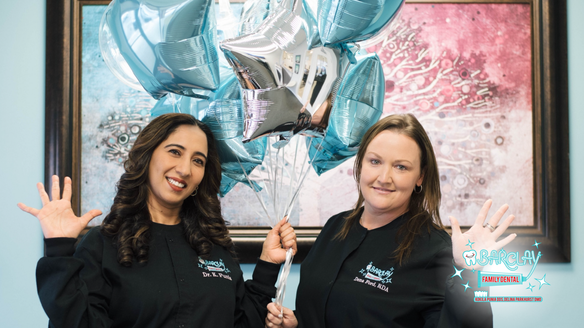 Two women are standing next to each other holding balloons in front of a painting.