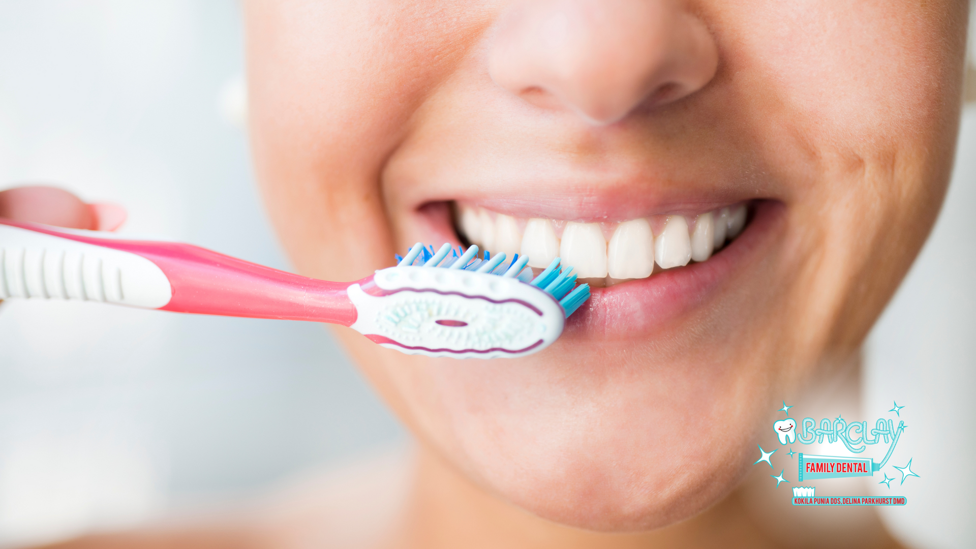 Person brushing teeth with pink and white toothbrush, smiling.