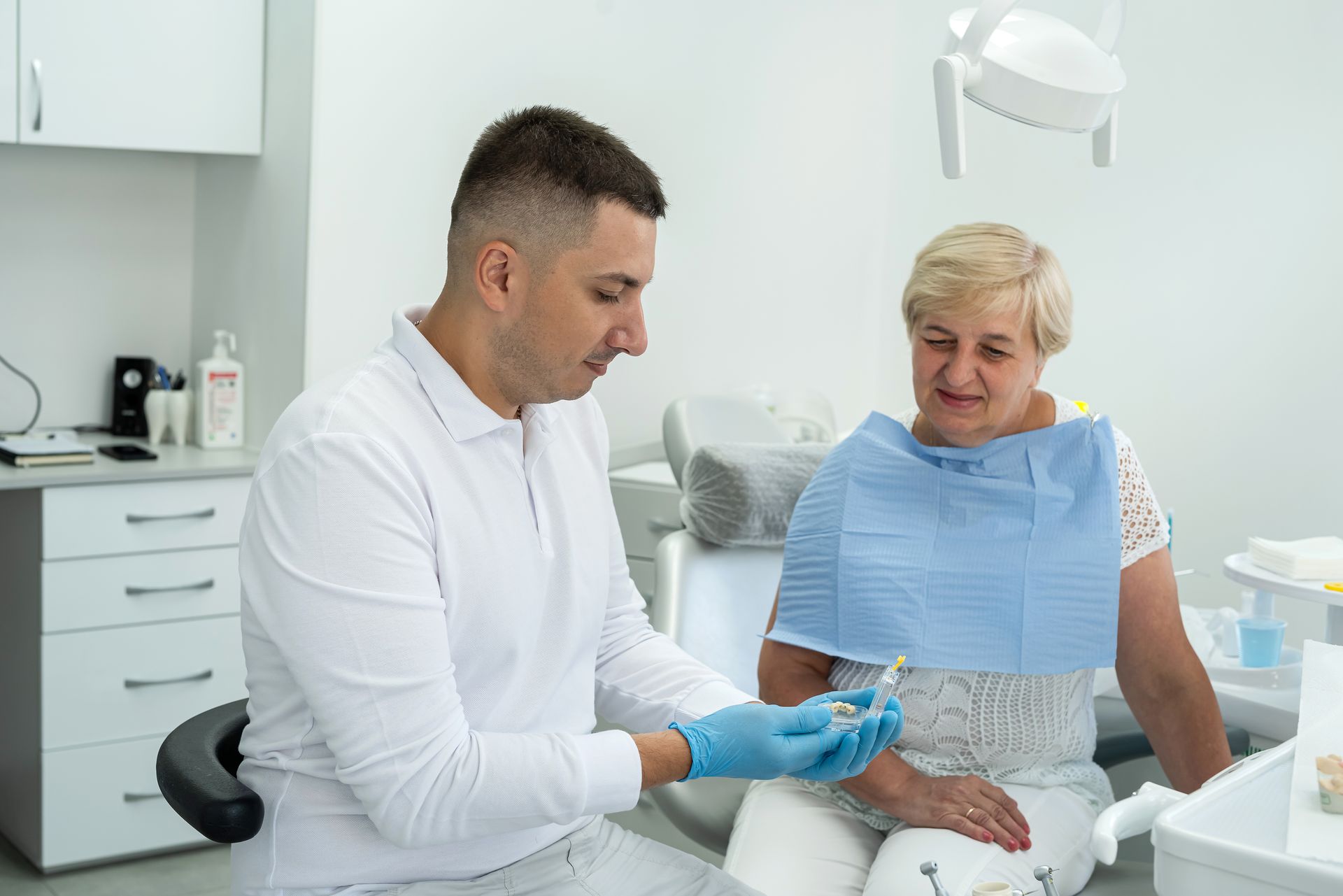 Dentist showing a dental implant to a seated patient in a bright dental office.