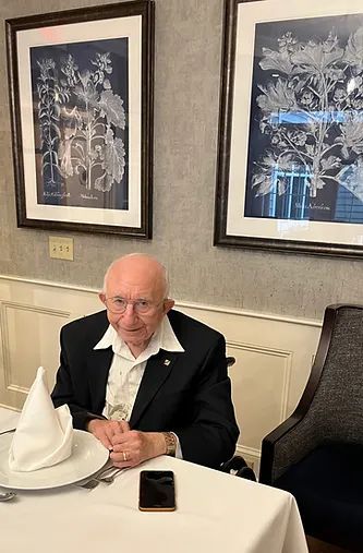 Man seated at a restaurant table with a folded napkin, smartphone, and framed wall art behind him