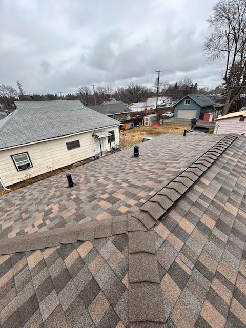 Roof shingles with vents and neighboring houses under a cloudy sky