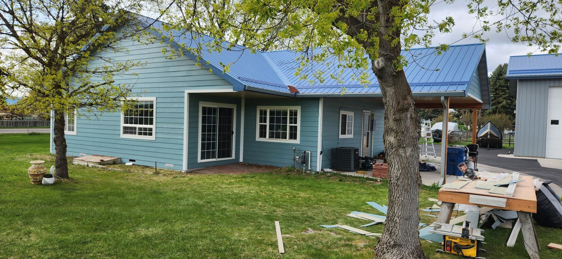 A blue-sided house with a blue roof, green lawn, and trees. Construction is in progress.