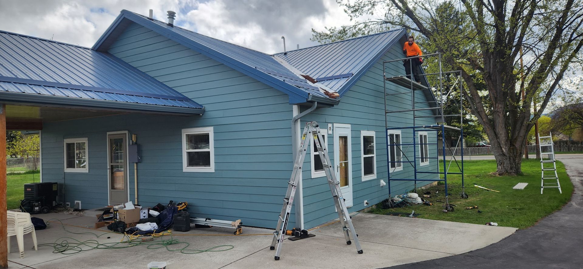 Workers on scaffolding installing a blue metal roof on a teal house.