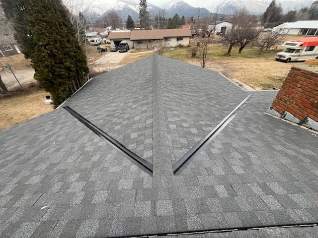 Rooftop with gray shingles and a central ridge, overlooking a suburban yard and distant mountains