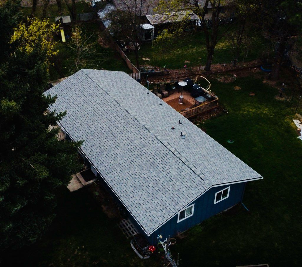 A blue house with a light gray roof seen from above, surrounded by trees and a backyard deck.