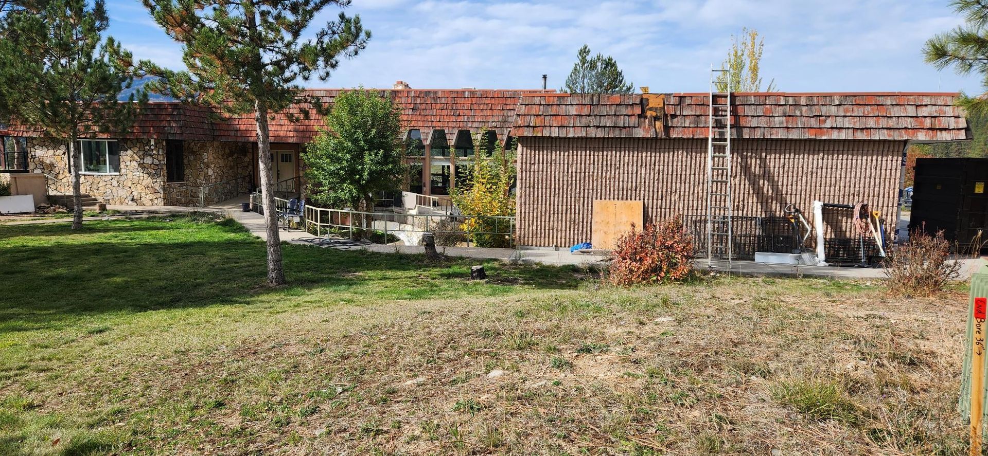 A building with a brick wall and red roof, surrounded by green grass and trees.