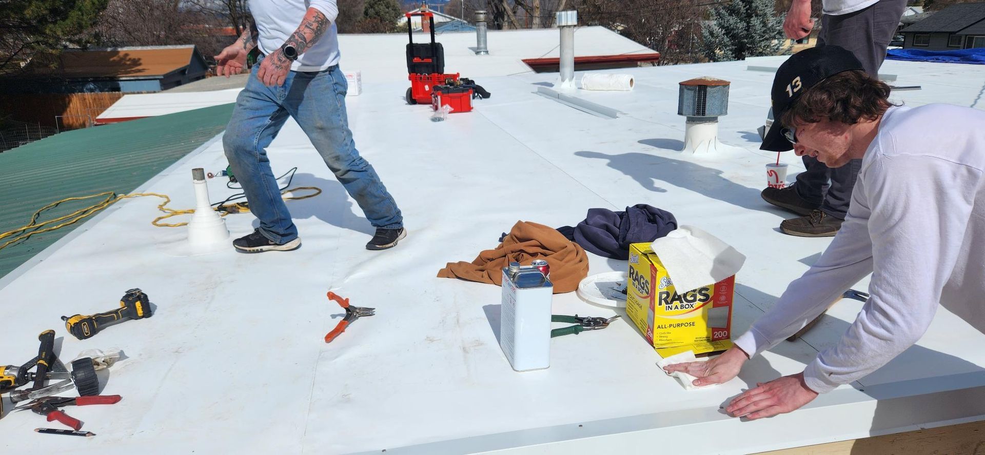 Workers on a white roof, applying sealant, surrounded by tools and materials.