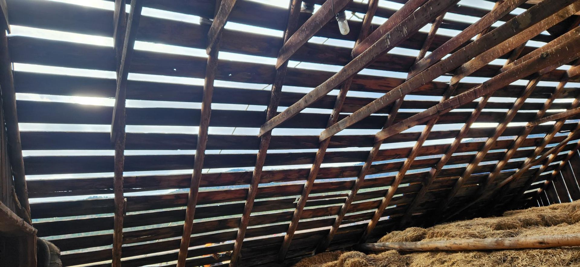 Inside of a dilapidated barn roof with sunlight shining through the gaps between the wooden planks.
