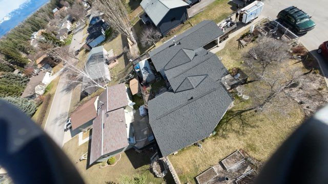 Aerial view of a residential neighborhood with rooftops, parked cars, and leafless trees.
