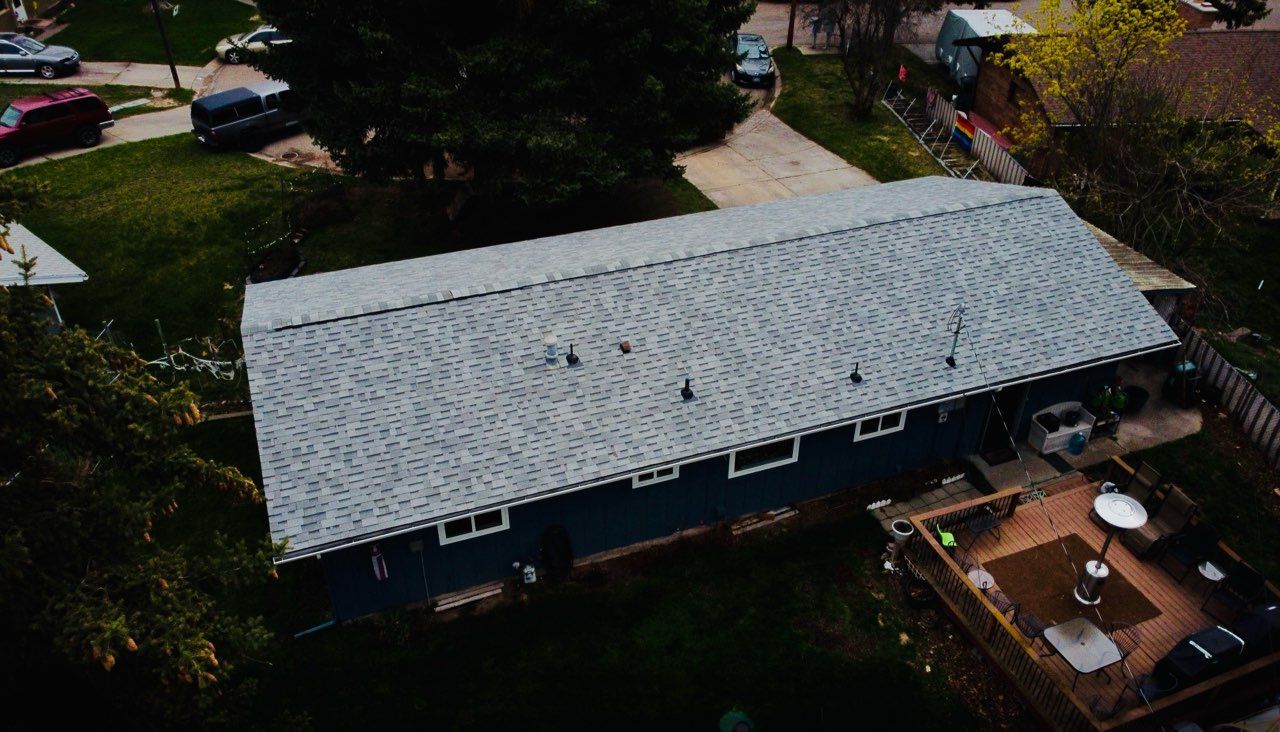 Aerial view of a blue house with a gray roof beside a wooden deck and trees.