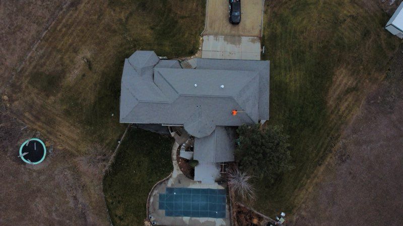 Aerial view of a house with a gray roof, backyard pool, and surrounding lawn.