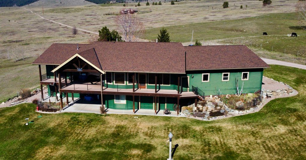 Rustic green lodge with brown roof in a grassy rural landscape, viewed from above