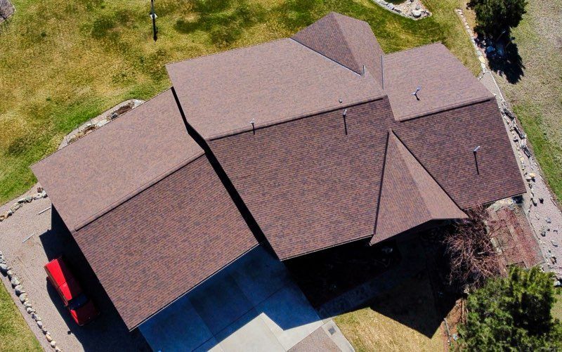 Aerial view of a house with a brown roof and a red vehicle parked beside it.