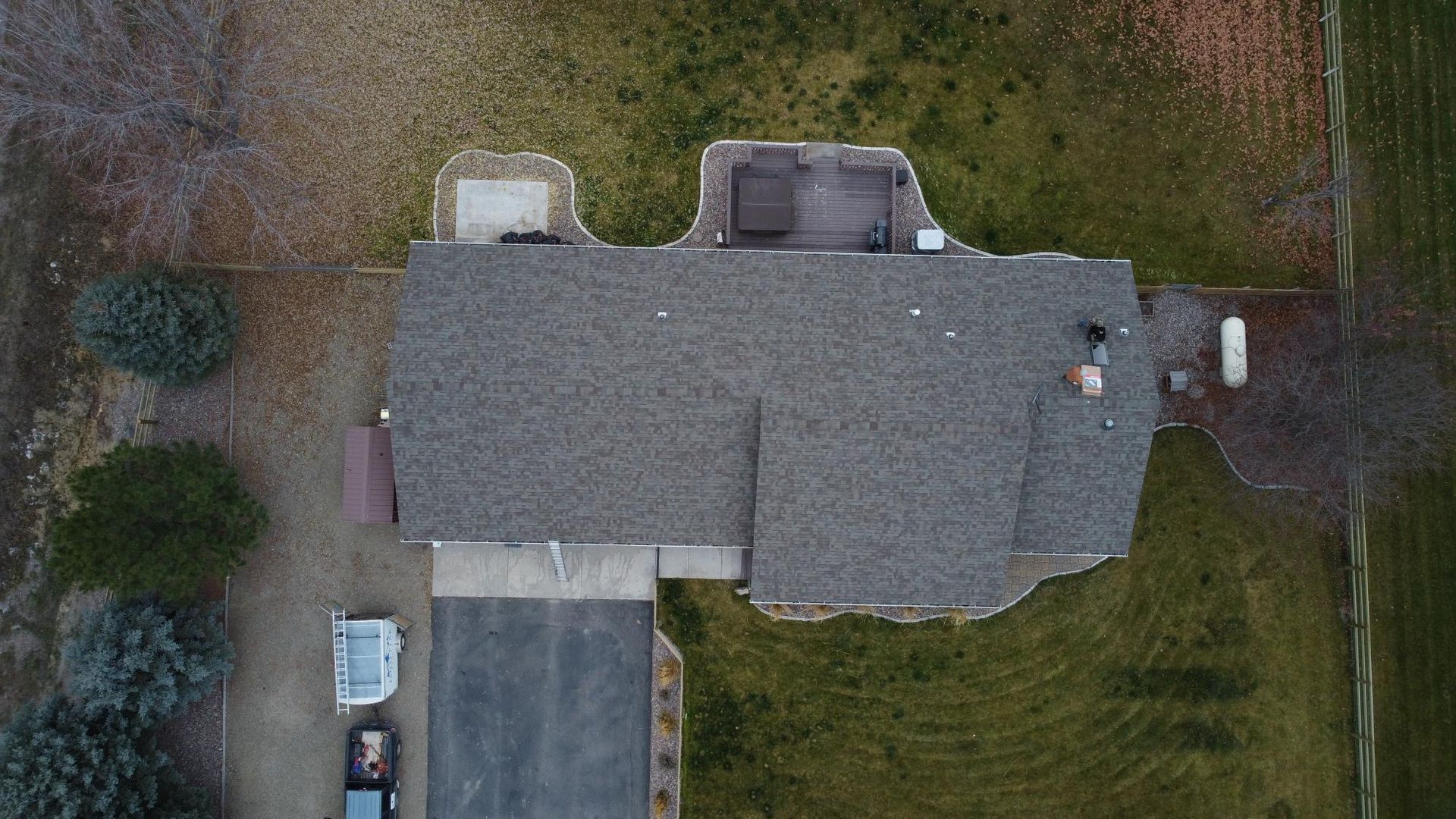 Overhead view of a house with a dark gray roof, surrounded by lawn and trees; a driveway is in the front.