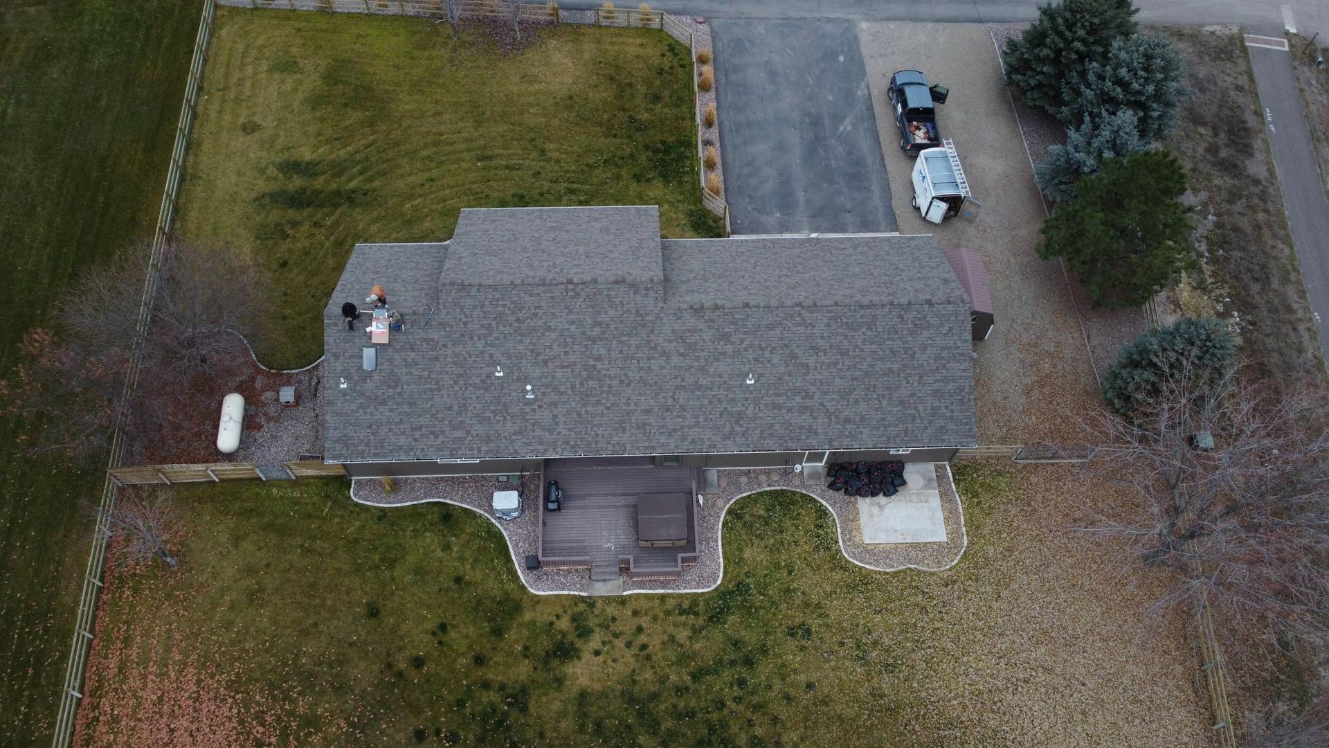 Overhead view of a house with a gray roof and a driveway. Green and brown lawn.
