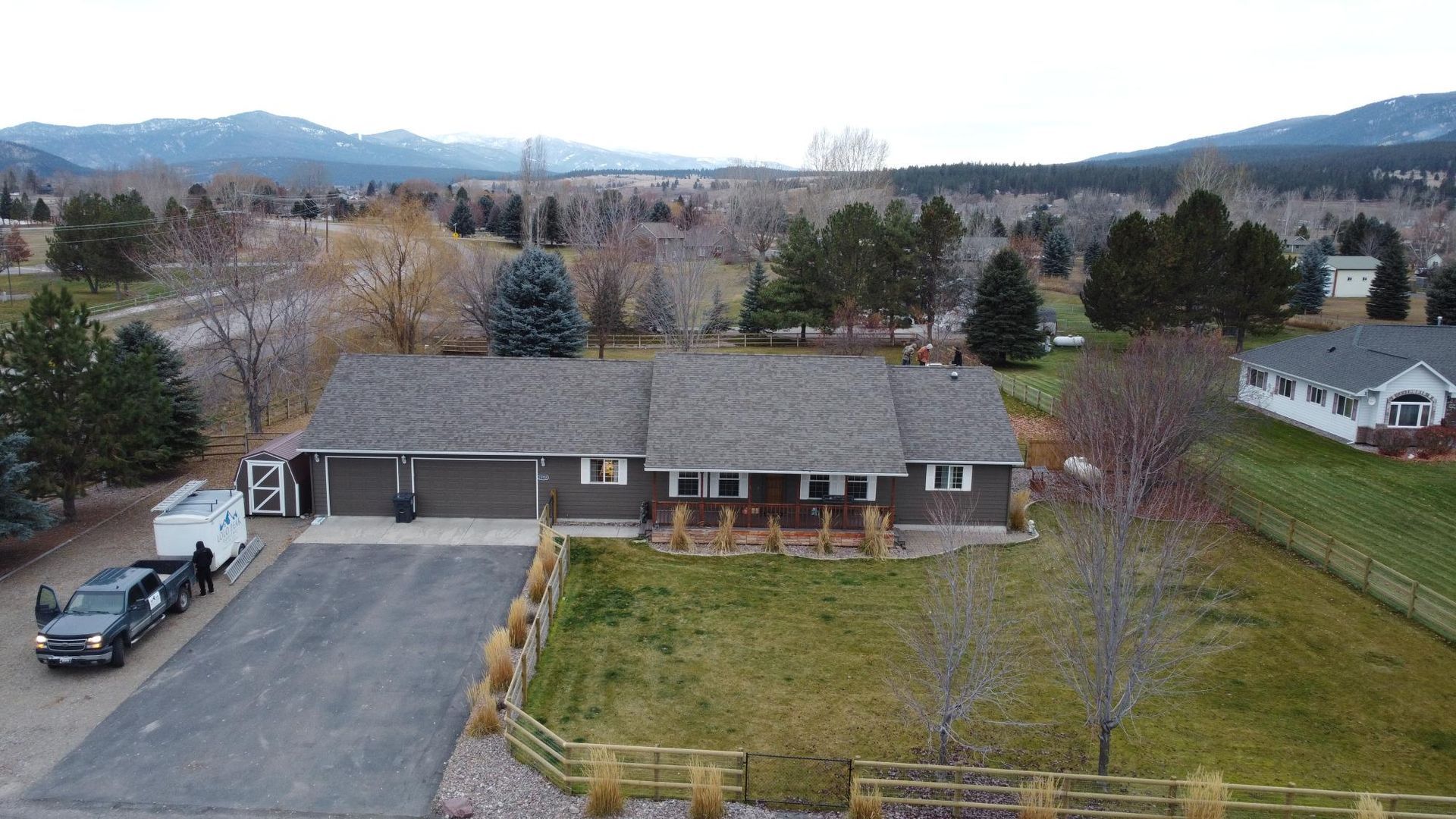 Aerial view of a gray house with a long driveway and a truck parked outside; mountains in the background.
