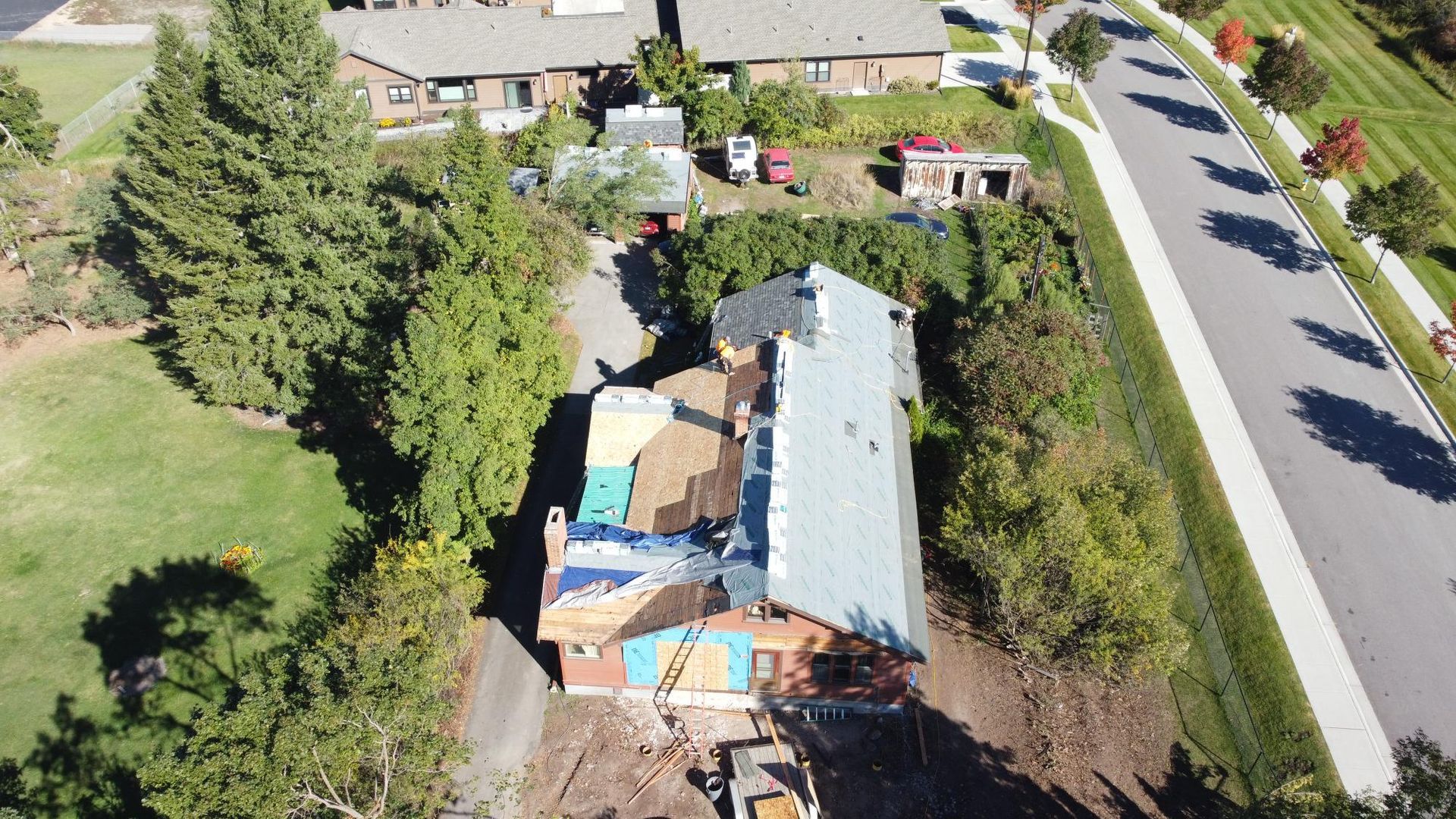 Aerial view of a house with roof damage, surrounded by trees and a driveway near a road.