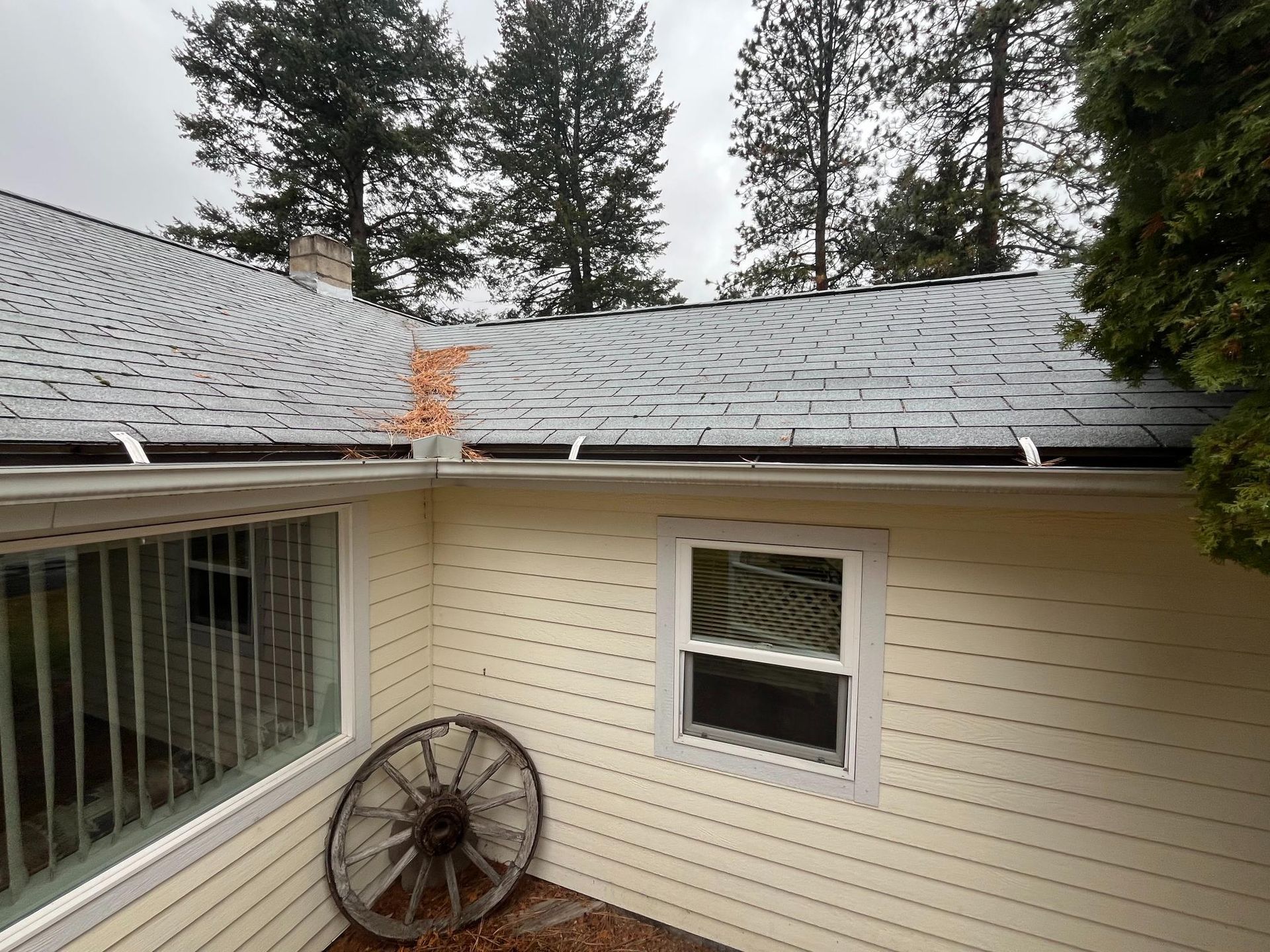 View of a light yellow house with dark gray roof, black gutters, and a large wooden wheel.