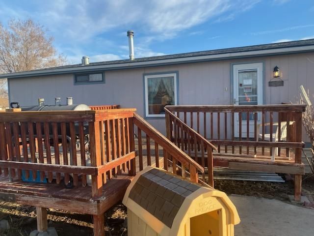 A light purple house with a wooden deck and a dog house in front. Blue sky.