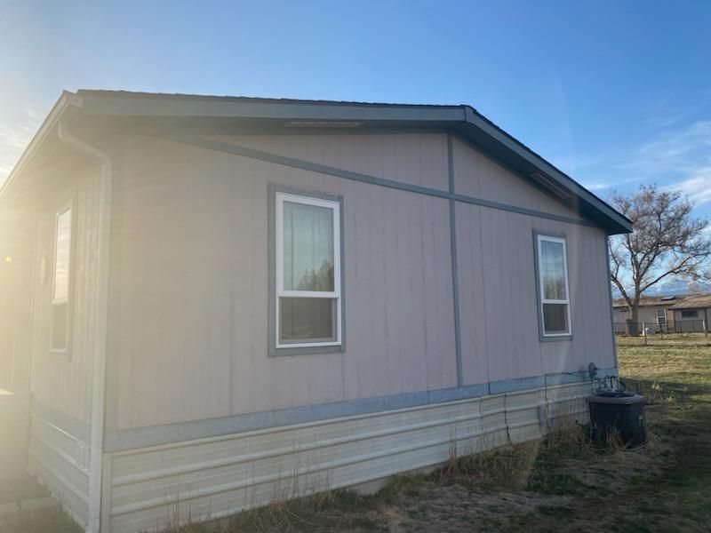 Side view of a light gray mobile home with white-trimmed windows against a blue sky.